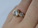 a woman ' s hand holding a gold ring with two diamonds