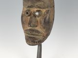 un masque en bois posé sur un socle, devant un fond blanc