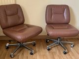une paire de fauteuils de bureau en cuir marron posés sur un parquet en bois massif