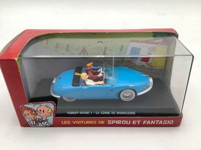 une petite voiture dans une boîte posée sur une surface blanche, avec une boîte rouge à côté