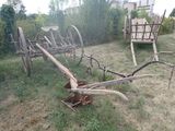 une charrue en bois posée dans l'herbe, à côté d'un chariot en bois