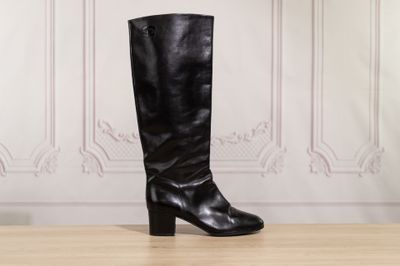 black leather boots on a wooden table in front of a white wall