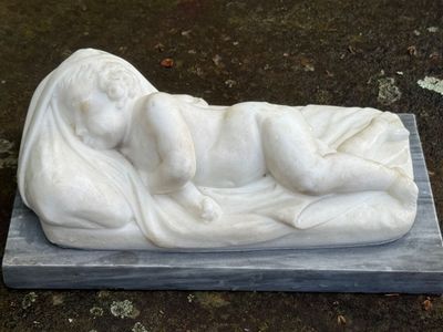 une statue blanche représentant un bébé allongé sur une couverture