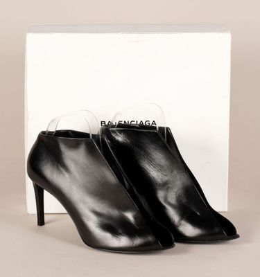 une paire de bottines en cuir noir posées devant une boîte blanche