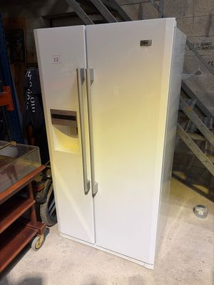 un réfrigérateur blanc posé dans un garage, à côté d'un escalier