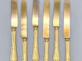 four gold plated knives and a knife on a white surface