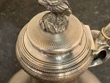 a silver teapot with a bird on top of it