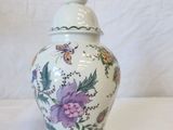 a white vase with purple flowers on it next to a measuring tape