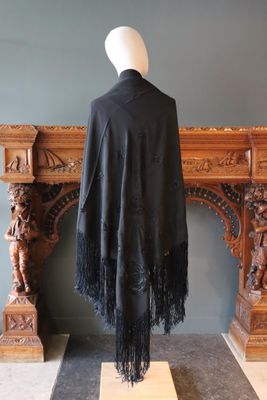 châle noir à franges sur un mannequin devant une cheminée