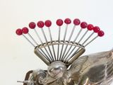 une sculpture en argent représentant un oiseau avec des perles rouges sur la tête