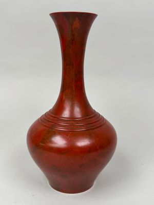 un vase rouge posé sur une surface blanche