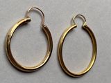 two pairs of gold hoop earrings sitting on top of a white surface