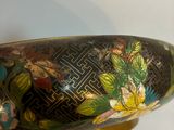 a black and gold bowl with flowers and leaves on it