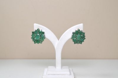 une paire de boucles d'oreilles vertes posées sur un présentoir blanc, sur une table blanche