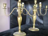 deux chandeliers en or posés sur une table, avec une horloge en arrière-plan