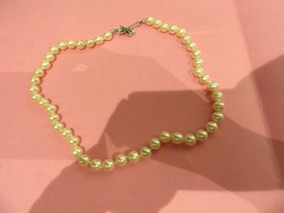 a pearl necklace on a pink surface with a shadow of a person