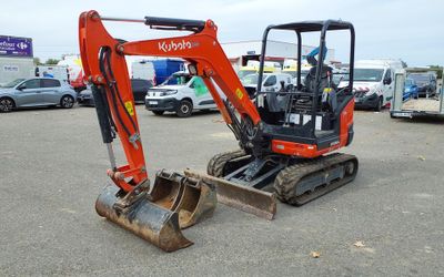 an orange excavator sitting in a parking lot with other vehicles in the background