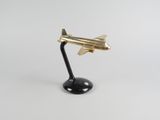 un petit avion doré posé sur un socle noir, sur une surface blanche