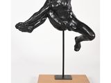 une sculpture noire représentant un homme, posée sur un socle en bois