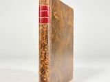 an old book with a red cover sitting on a white surface