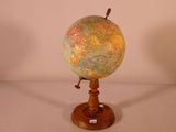 un petit globe posé sur un socle en bois, lui-même posé sur une surface blanche
