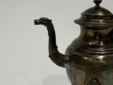 a silver tea pot on a stand on a white surface