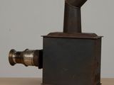 a small metal stove on a wooden table with a white wall in the background