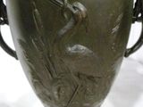 a green vase with a bird on it on a table
