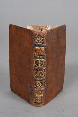 an old brown book with gold trim sitting on top of a table