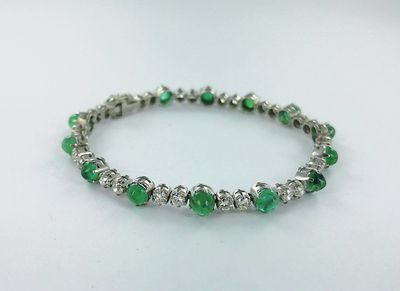 un gros plan d'un bracelet orné de pierres vertes sur un fond blanc