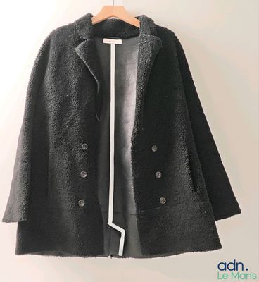 black coat with white trims hanging on a hanger on a wall