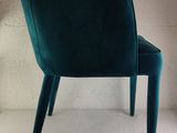 the back of a green velvet chair with wooden legs and a white background