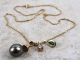 a close up of a necklace with a black pearl and a green stone