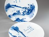 two blue and white plates with designs of mountains and trees on them