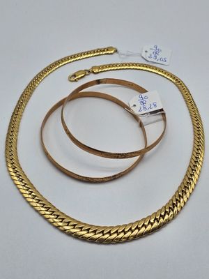 un gros plan d'un collier et d'un bracelet en or posés sur une surface blanche