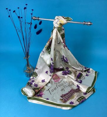 a white scarf with purple flowers on it next to a vase with purple flowers