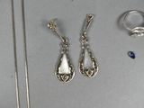 two pairs of silver earrings and a necklace on a table