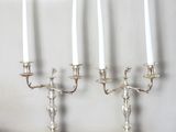 trois chandeliers en argent avec des bougies blanches posés sur une table en bois