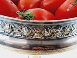 a silver bowl filled with tomatoes on top of a table
