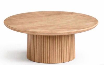 La table est en bois et possède un piètement rond.