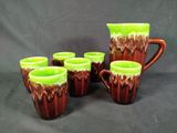 six green and brown coffee mugs and a pitcher on a black background