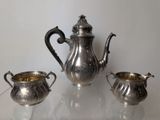a silver tea pot and two silver cups on a glass table