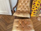 fauteuil et repose-pieds en cuir marron dans une pièce aux murs recouverts d'un papier peint à motifs de paons