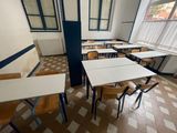 tables and chairs in an empty classroom with a refrigerator in the background