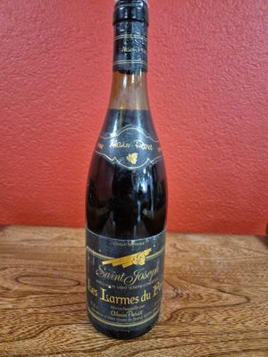 an empty bottle of wine sitting on a wooden table in front of a red wall