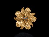 une photo d'une broche en forme de fleur en or sertie de pierres bleues