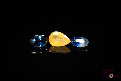 two blue and one yellow sapphires on a black surface