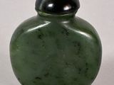 a green vase with a black lid sitting on a white surface