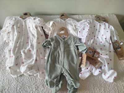 several baby clothes are laid out on a bed in a row
