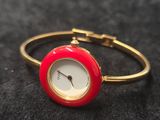 une image représentant une montre-bracelet rouge et dorée posée sur une surface noire
